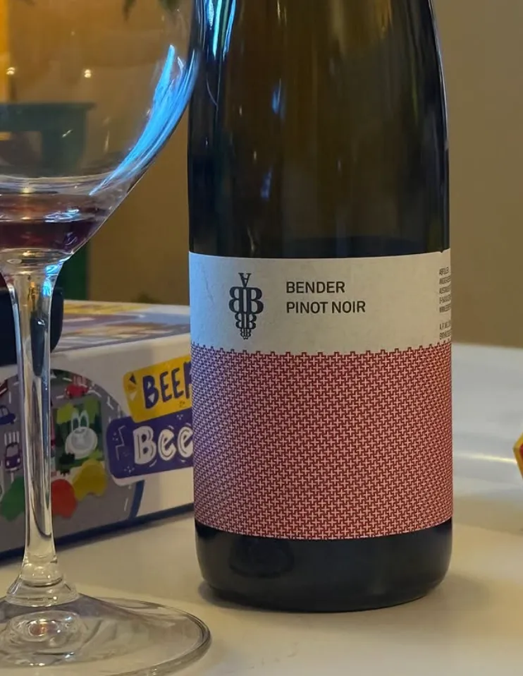 Botella del Andreas Bender Pinot Noir 2024, tinto alemán del Pfalz, con su etiqueta blanca y roja de tramado junto a una copa de vino tinto casi vacía.