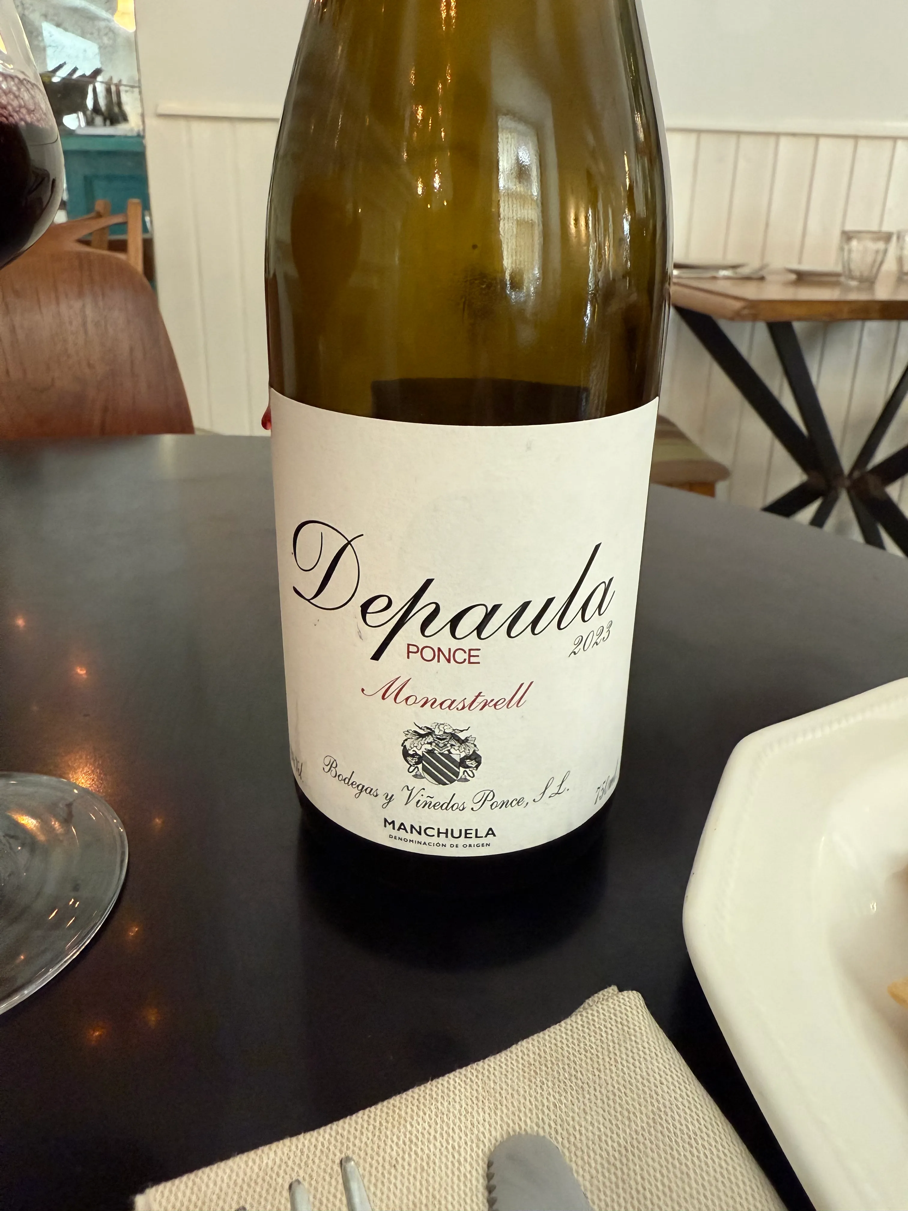 Botella del DePaula 2023 de Bodegas Ponce, una Monastrell de la Manchuela, sobre una mesa junto a una copa de tinto servida.