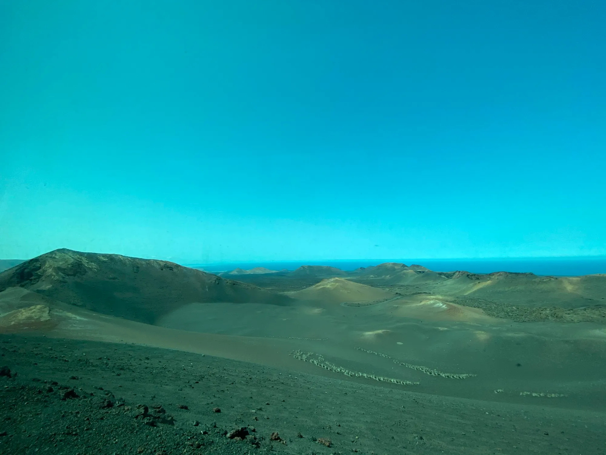 Volcanic landscape of Timanfaya National Park, Lanzarote: cones and craters of ash and lapilli across a black-and-rust desert, with the Atlantic on the horizon under a clear sky.